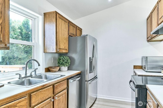 kitchen featuring stainless steel appliances, a sink, brown cabinetry, and healthy amount of natural light