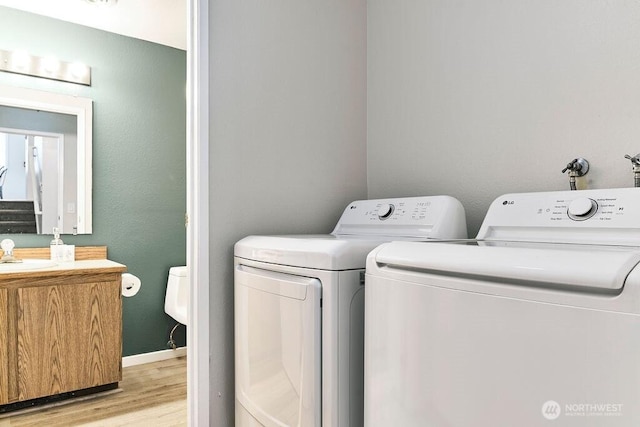 laundry area featuring light wood-style floors, independent washer and dryer, a sink, and baseboards