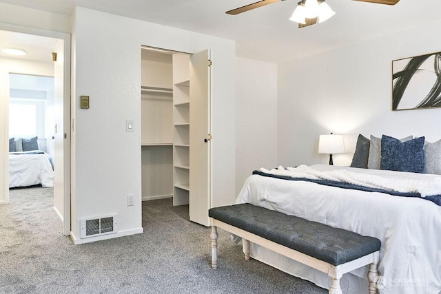 carpeted bedroom featuring a walk in closet, a ceiling fan, and baseboards
