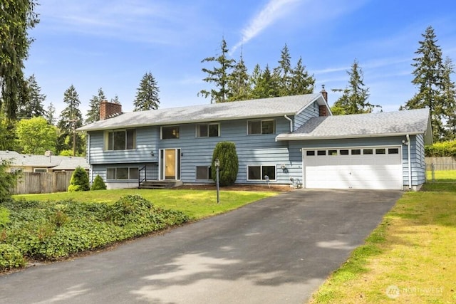 bi-level home with a chimney, an attached garage, and asphalt driveway