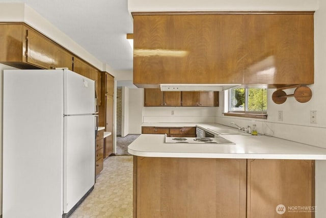kitchen with freestanding refrigerator, a sink, a peninsula, light countertops, and light flooring