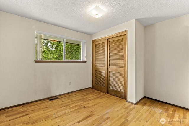 unfurnished bedroom featuring light wood-style flooring, a closet, a textured ceiling, and baseboards