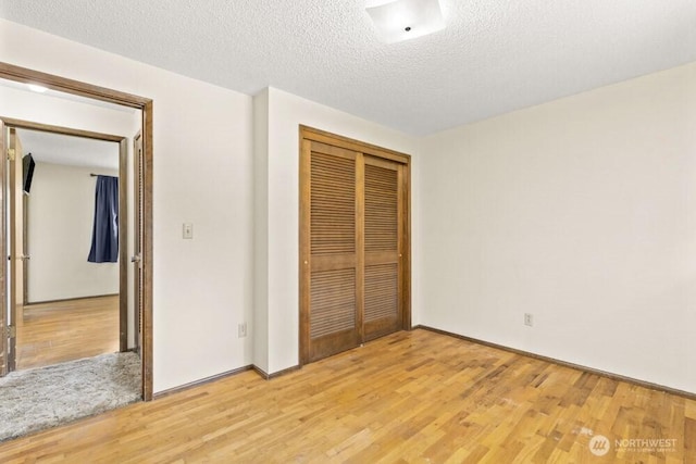 unfurnished bedroom featuring light wood-style floors, a closet, a textured ceiling, and baseboards
