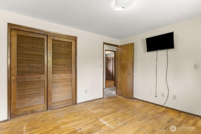 unfurnished bedroom with light wood finished floors, a closet, a textured ceiling, and baseboards