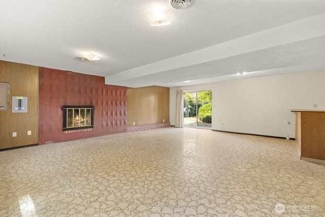 unfurnished living room featuring a textured ceiling, baseboards, a fireplace, and wooden walls