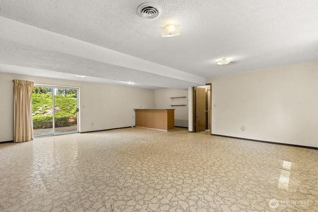 unfurnished living room featuring baseboards, a textured ceiling, bar area, and light stone finish floors