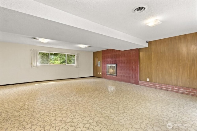 unfurnished room with wood walls, a glass covered fireplace, baseboards, and a textured ceiling
