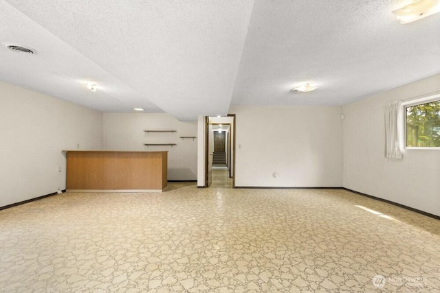 unfurnished living room featuring bar area, baseboards, and a textured ceiling