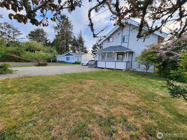 view of green lawn featuring gravel driveway and a sunroom
