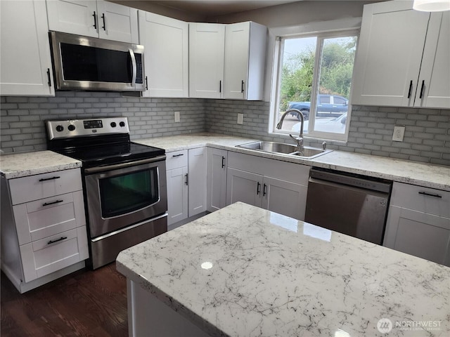 kitchen with appliances with stainless steel finishes, a sink, dark wood-style flooring, backsplash, and light stone countertops