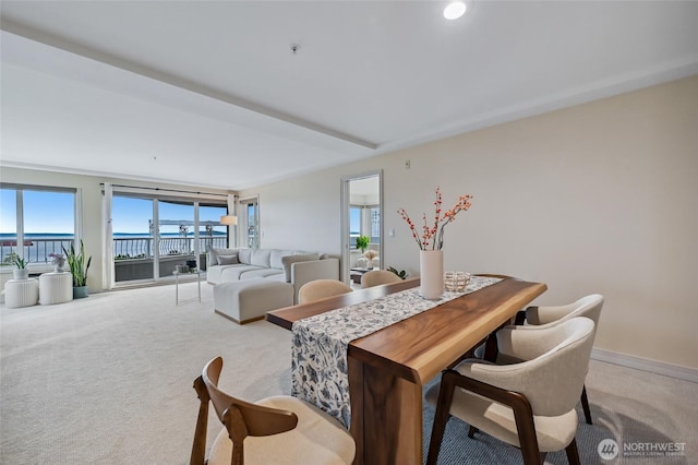 dining space with light carpet, a water view, and baseboards