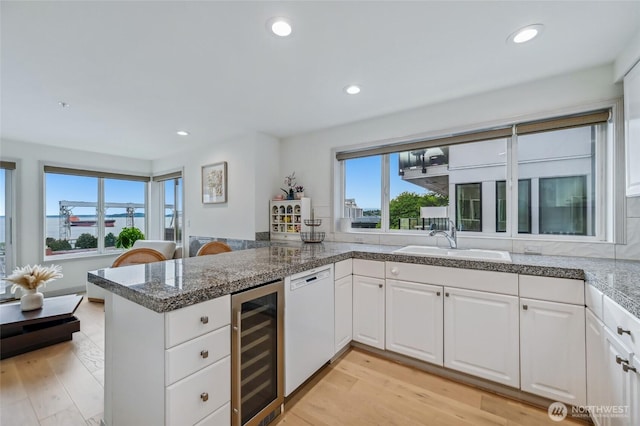 kitchen with beverage cooler, a sink, a peninsula, dishwasher, and white cabinetry