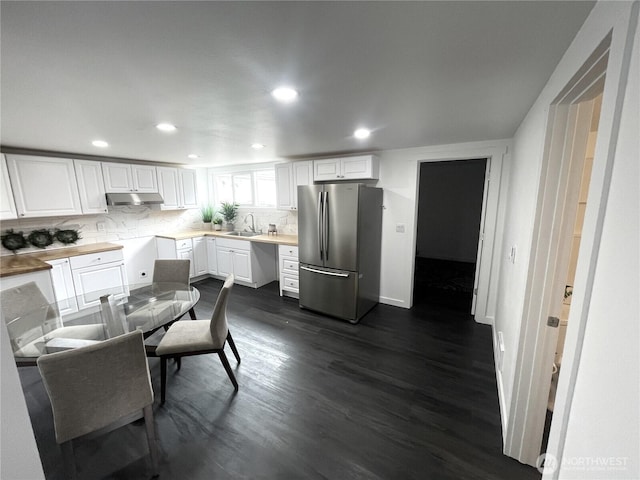 kitchen with freestanding refrigerator, a sink, dark wood-type flooring, white cabinets, and under cabinet range hood