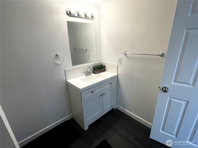 bathroom with baseboards, vanity, wood finished floors, and tasteful backsplash