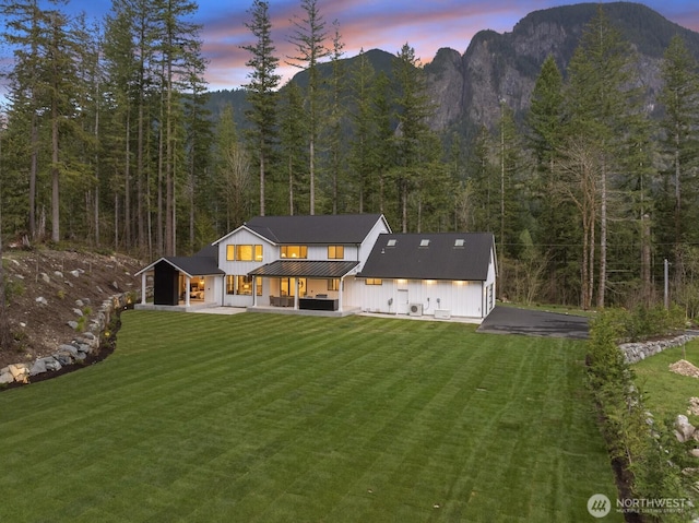 6993 N Fork Rd SE, Snoqualmie, WA 98065 - back of house at dusk with a wooded view, board and batten siding, a lawn, metal roof, and a patio area