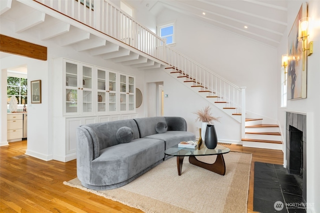 living room featuring stairway, wood finished floors, high vaulted ceiling, a fireplace with flush hearth, and baseboards