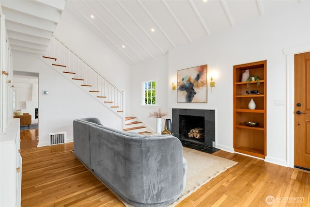 living area with a tile fireplace, stairs, light wood-style flooring, built in features, and baseboards