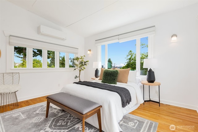 bedroom featuring a wall mounted AC, wood finished floors, and baseboards