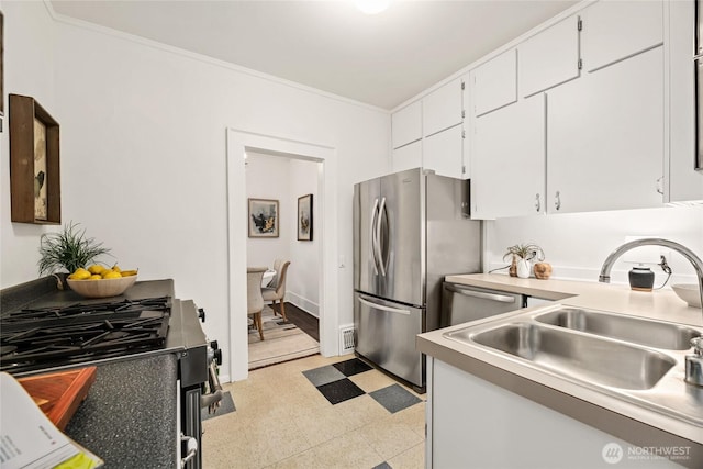 kitchen featuring appliances with stainless steel finishes, a sink, white cabinets, ornamental molding, and light flooring