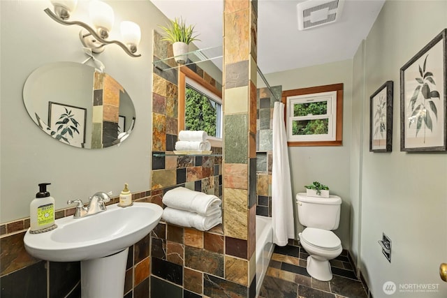 full bathroom with stone tile flooring, toilet, and shower / tub combo with curtain