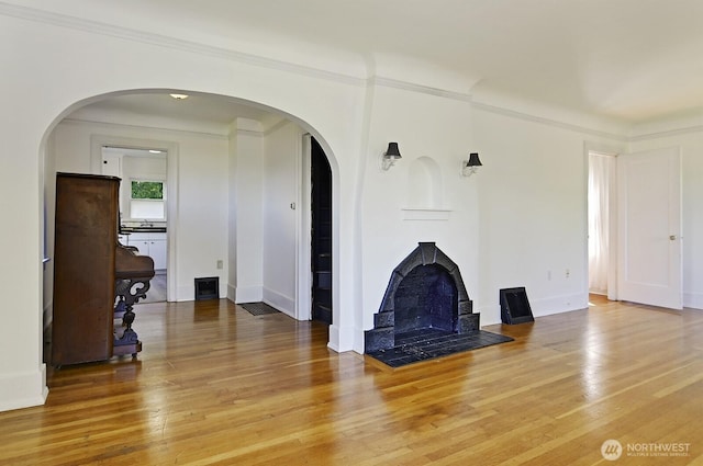 unfurnished living room featuring arched walkways, wood finished floors, baseboards, and crown molding