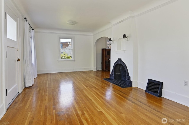 unfurnished living room featuring arched walkways, light wood-style floors, and baseboards