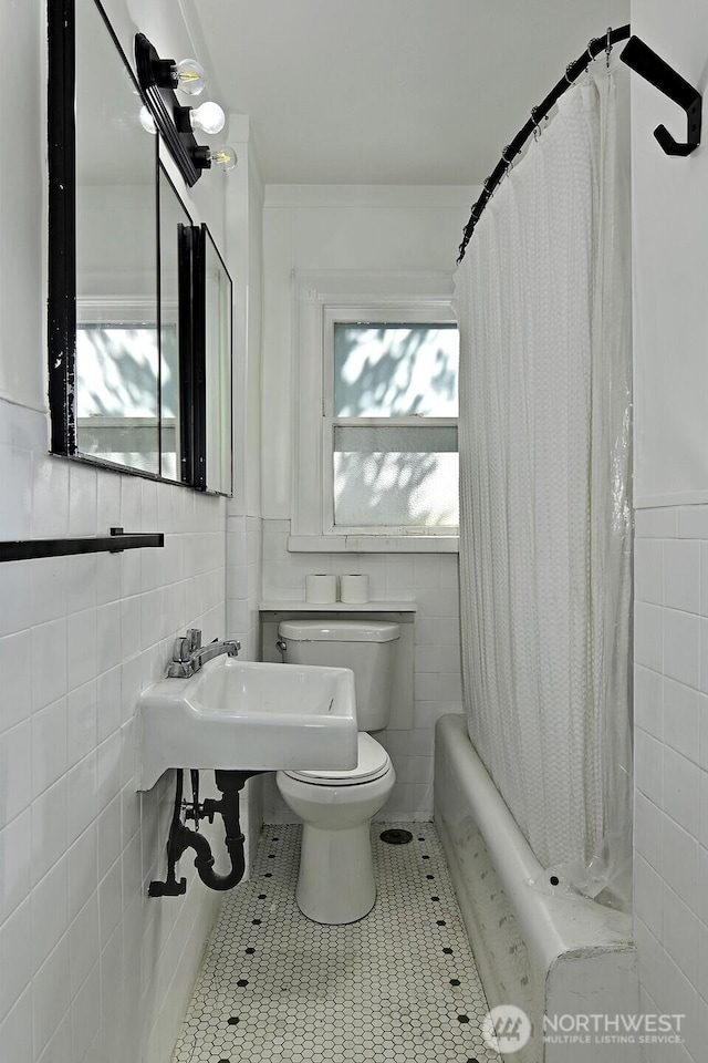 full bathroom featuring tile walls, toilet, tile patterned flooring, wainscoting, and a sink