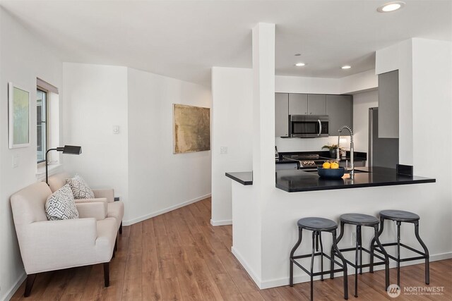 1125 E Olive St Unit 501, Seattle, WA 98122 - kitchen featuring stainless steel appliances, gray cabinets, a kitchen bar, dark countertops, and wood finished floors