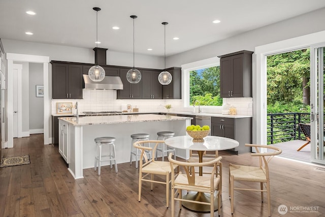 kitchen featuring an island with sink, tasteful backsplash, dark wood-style flooring, extractor fan, and recessed lighting