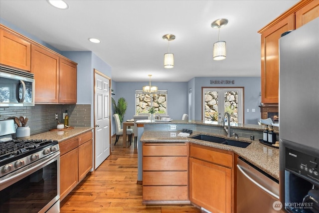kitchen featuring stainless steel appliances, a sink, backsplash, light wood-type flooring, and light stone countertops
