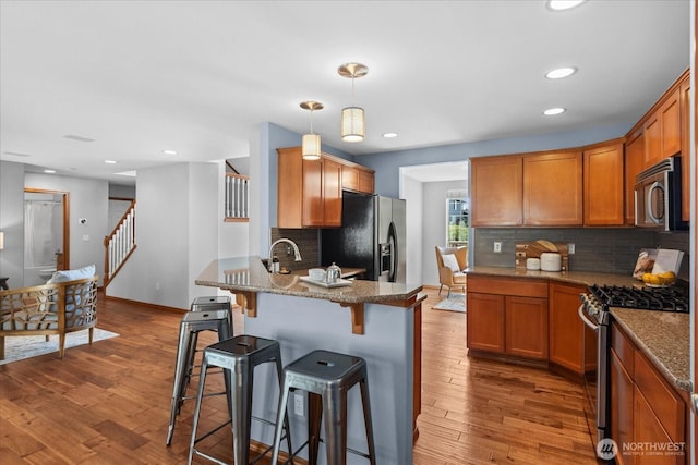 kitchen with stainless steel appliances, a peninsula, tasteful backsplash, a kitchen bar, and stone countertops