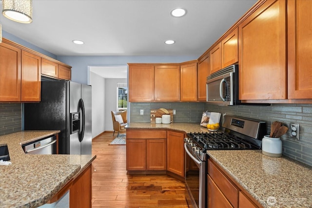kitchen with appliances with stainless steel finishes, light wood-type flooring, tasteful backsplash, light stone countertops, and brown cabinets