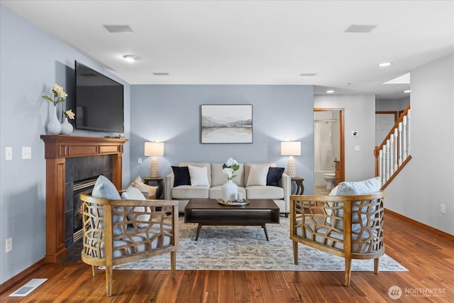 living room featuring wood finished floors, baseboards, stairway, recessed lighting, and a tiled fireplace