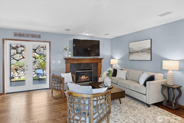 living area with wood finished floors, french doors, and a tile fireplace