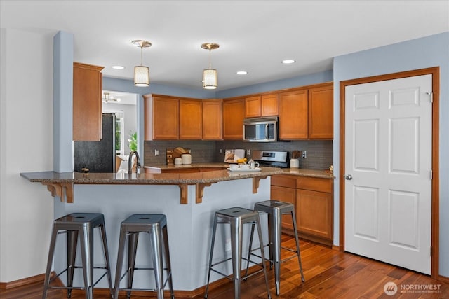 kitchen featuring appliances with stainless steel finishes, a peninsula, a breakfast bar area, decorative backsplash, and recessed lighting