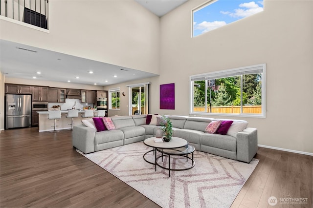 living room with dark wood-style flooring, a towering ceiling, recessed lighting, and baseboards