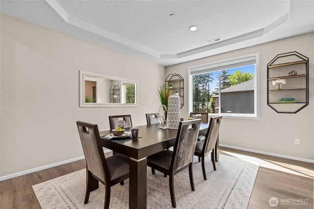 dining room with a tray ceiling, baseboards, wood finished floors, and recessed lighting