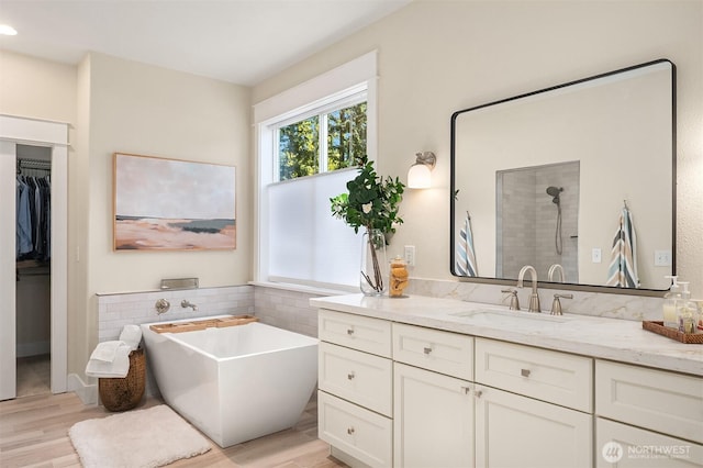 full bath featuring wood finished floors, vanity, a tile shower, a freestanding bath, and a spacious closet