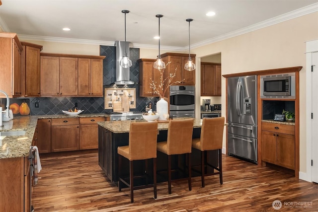 kitchen with stainless steel appliances, wall chimney range hood, brown cabinets, dark wood-style floors, and ornamental molding
