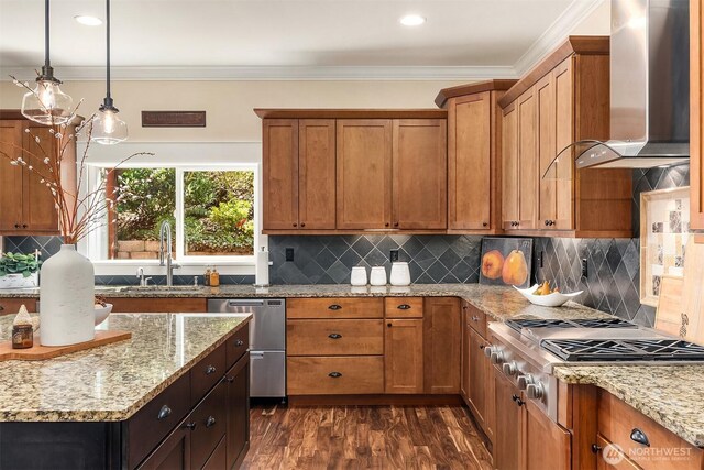 kitchen with wall chimney exhaust hood, a sink, appliances with stainless steel finishes, brown cabinetry, and crown molding