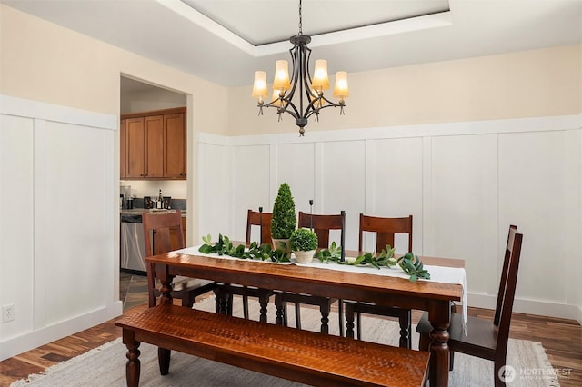 dining area featuring a chandelier, a decorative wall, wood finished floors, and a tray ceiling