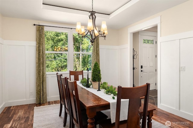dining area with a decorative wall, a chandelier, dark wood finished floors, a wainscoted wall, and a raised ceiling