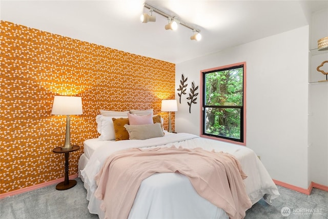 bedroom with an accent wall, track lighting, wallpapered walls, carpet flooring, and baseboards