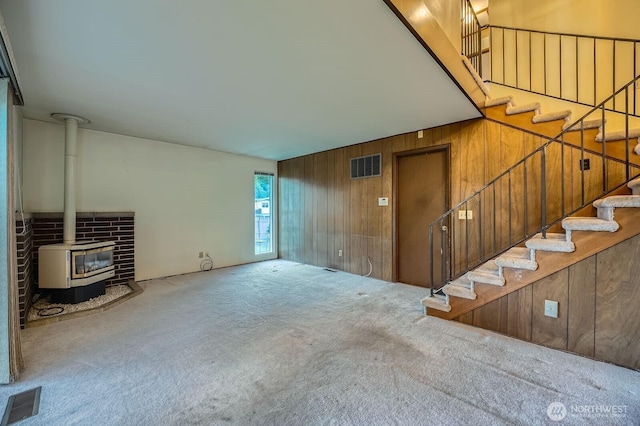 23238 21st Ave S, Des Moines, WA 98198 - unfurnished living room featuring a wood stove, wood walls, carpet floors, and stairs
