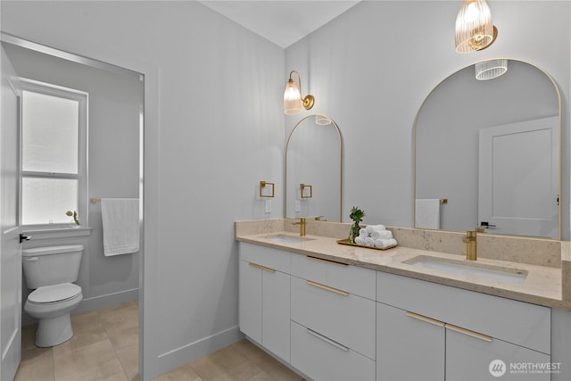 bathroom featuring toilet, double vanity, and baseboards
