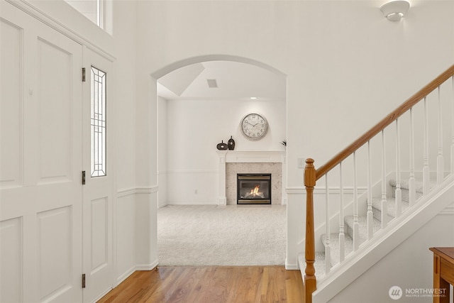 entrance foyer with wood finished floors, arched walkways, a high ceiling, a tile fireplace, and stairs