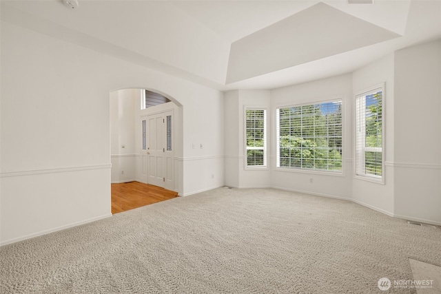 carpeted spare room with arched walkways and baseboards