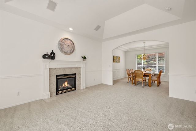 carpeted living area featuring arched walkways, a fireplace, wainscoting, recessed lighting, and a chandelier