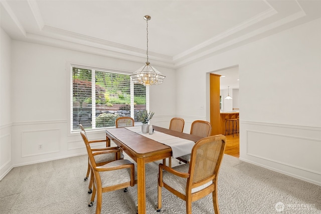 dining area with a raised ceiling, a chandelier, light colored carpet, crown molding, and wainscoting