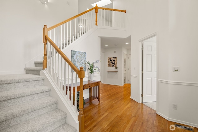 staircase featuring wood finished floors, a high ceiling, baseboards, and recessed lighting